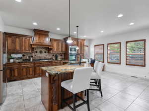 Kitchen with dark stone counters, a kitchen breakfast bar, pendant lighting, a center island with sink, and stainless steel appliances