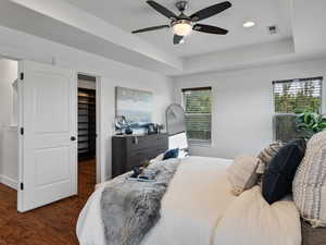 Bedroom with a raised ceiling, a walk in closet, dark wood-style flooring, ceiling fan, and recessed lighting