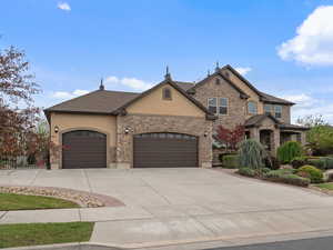 View of front of home with stucco siding, driveway, an attached garage, and stone siding