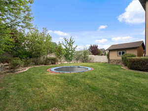Fenced backyard featuring a trampoline