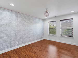 Empty room featuring brick wall, dark wood-style floors, and a chandelier