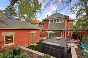 Back of house with a hot tub, a patio, brick siding, and a shingled roof