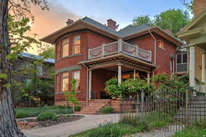 Victorian-style house featuring a fenced front yard, brick siding, a chimney, a balcony, and a gate