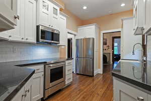 Kitchen with stainless steel appliances, dark stone counters, decorative backsplash, white cabinets, and recessed lighting