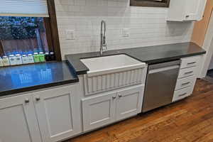 Kitchen featuring white cabinets, dark stone countertops, dishwasher, and dark wood finished floors