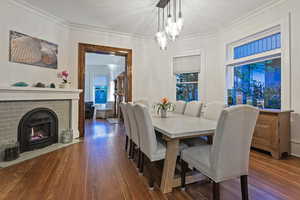 Dining room featuring hardwood / wood-style floors, a brick fireplace, hanging lights, and crown molding