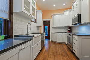 Kitchen with glass fronted cabinets, dark wood finished floors, white cabinetry, and recessed lighting