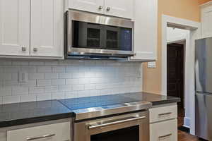 Kitchen featuring stainless steel appliances, white cabinets, tasteful backsplash, and dark stone countertops