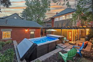 Back of house with a hot tub, a patio, roof with shingles, a pergola, and brick siding