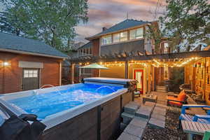 Rear view of house featuring a hot tub, a pergola, a patio, roof with shingles, and brick siding