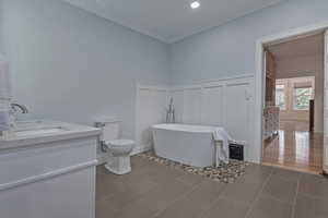 Full bath featuring a freestanding tub, a decorative wall, vanity, crown molding, and wainscoting