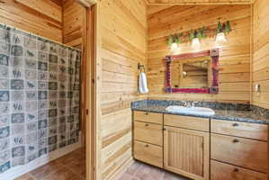 Bathroom with wooden walls, curtained shower, vanity, and light tile patterned floors