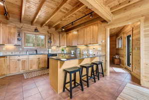 Kitchen with track lighting, open shelves, a breakfast bar, a wooden ceiling with exposed beams, and wooden walls