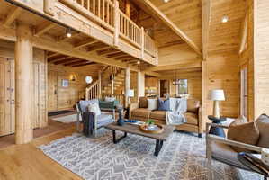 Living room with wooden walls, hardwood / wood-style floors, hanging lights, and a high wooden beamed ceiling