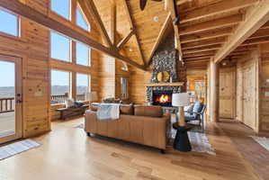 Living area with wooden walls, a high wooden beamed ceiling, wood finished floors, and a stone fireplace