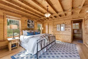 Bedroom with multiple windows, wooden walls, a wooden ceiling with exposed beams, and light wood-style floors