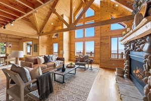 Living room with light wood-style flooring, a high wood beamed ceiling, plenty of natural light, a fireplace, and wood walls