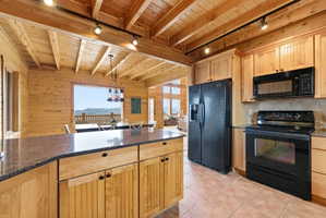 Kitchen with wood walls, black appliances, dark stone counters, light wood finish cabinets, and hanging lights