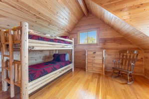 Bedroom with a wooden ceiling with exposed beams, light wood-style flooring, and wooden walls