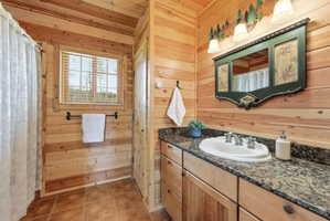 Full bath with wood walls, curtained shower, vanity, and light tile patterned flooring
