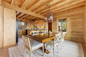 Dining room featuring wood walls, a wood ceiling with exposed beams, hanging lights, and light tile patterned floors