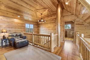 Living area with healthy amount of natural light, an upstairs landing, light wood finished floors, hanging lights, and wood ceiling