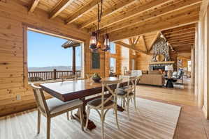 Dining room with wooden walls, a high wooden beamed ceiling, a chandelier, an outdoor stone fireplace, and a mountain view
