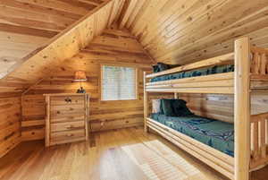 Bedroom featuring light wood-style flooring, a wood ceiling with exposed beams, and wood walls