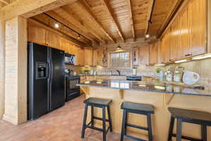 Kitchen with dark stone countertops, black appliances, a peninsula, rail lighting, and a breakfast bar area