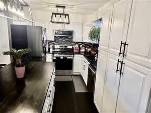 Kitchen with stainless steel appliances, dark countertops, white cabinetry, and hanging light fixtures