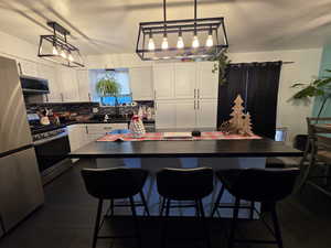 Kitchen with white cabinetry, stainless steel appliances, decorative backsplash, a kitchen bar, and a textured ceiling