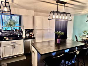 Kitchen with white cabinets, decorative backsplash, stainless steel dishwasher, decorative light fixtures, and a breakfast bar area