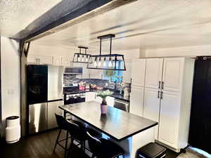 Kitchen featuring stainless steel appliances, decorative backsplash, white cabinets, a breakfast bar, and pendant lighting