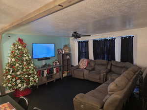 Living area with a ceiling fan, a textured ceiling, and dark wood-type flooring