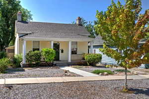 View of front of home featuring a chimney, covered porch, stucco siding, and a shingled roof