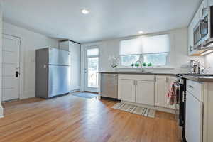 Kitchen with stainless steel appliances, white cabinetry, light wood-style flooring, dark countertops, and recessed lighting