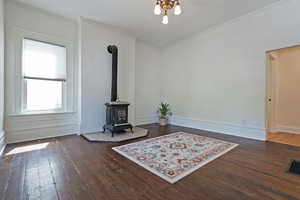 Living area with a wood stove, dark wood-type flooring, and crown molding