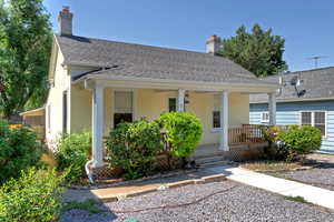 View of front of house with covered porch, stucco siding, a chimney, and a shingled roof