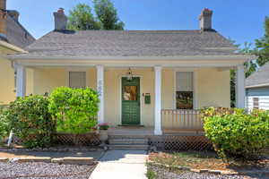 Property entrance with roof with shingles, a chimney, stucco siding, and covered porch