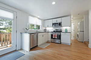 Kitchen featuring stainless steel appliances, white cabinetry, light wood-type flooring, stacked washer and dryer, and recessed lighting