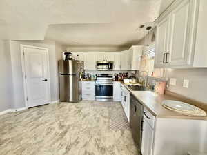Kitchen with stainless steel appliances, white cabinetry, light countertops, a textured ceiling, and hanging light fixtures