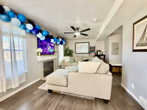 Living area featuring ceiling fan, wood finished floors, a glass covered fireplace, electric panel, and a textured ceiling