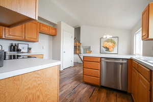 Kitchen featuring a peninsula, light countertops, stainless steel dishwasher, dark wood-type flooring, and suspended lighting