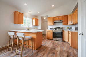 Kitchen with a kitchen breakfast bar, a peninsula, light countertops, stainless steel electric range, and dark wood finished floors