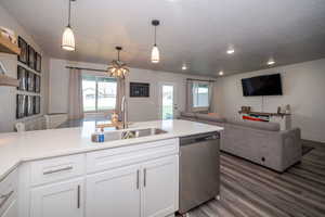 Kitchen with white cabinetry, open floor plan, dishwasher, a chandelier, and light stone counters