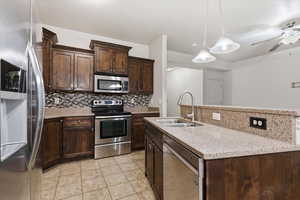 Kitchen featuring dark wood finish cabinets, stainless steel appliances, a kitchen island with sink, decorative backsplash, and light stone countertops