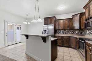 Kitchen featuring dark wood finish cabinetry, stainless steel appliances, light tile patterned floors, and a textured ceiling