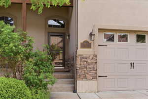 Property entrance with stucco siding, stone siding, and a garage