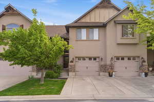 View of front of property featuring board and batten siding, driveway, a garage, stone siding, and stucco siding