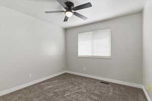 Empty room featuring dark colored carpet and a ceiling fan